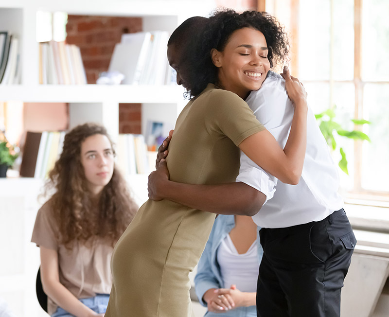 Woman psychologist addiction counsellor hugging supporting guy at group session